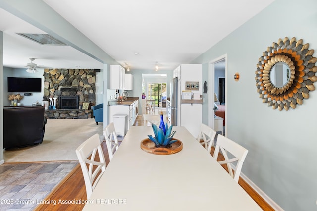 dining space with ceiling fan and a stone fireplace