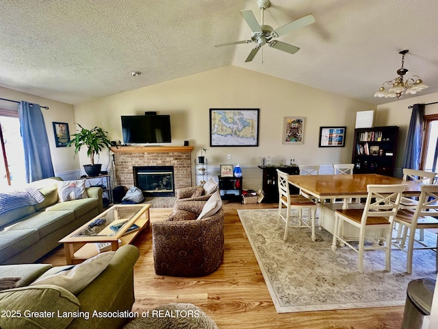 living area with wood finished floors, ceiling fan with notable chandelier, a fireplace, a textured ceiling, and lofted ceiling