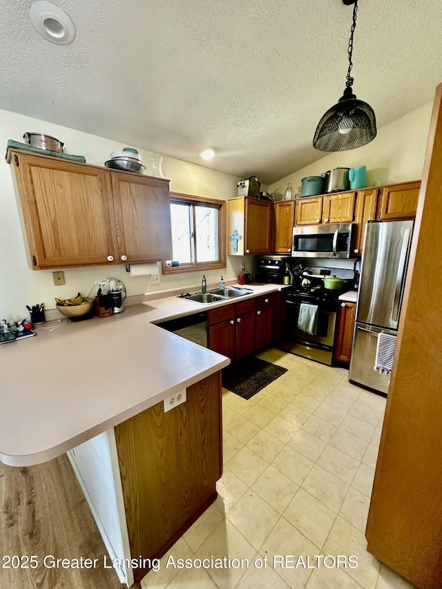 kitchen featuring a sink, a peninsula, light countertops, a textured ceiling, and appliances with stainless steel finishes