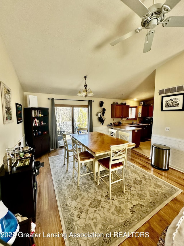 dining area with lofted ceiling, visible vents, wood finished floors, and ceiling fan with notable chandelier