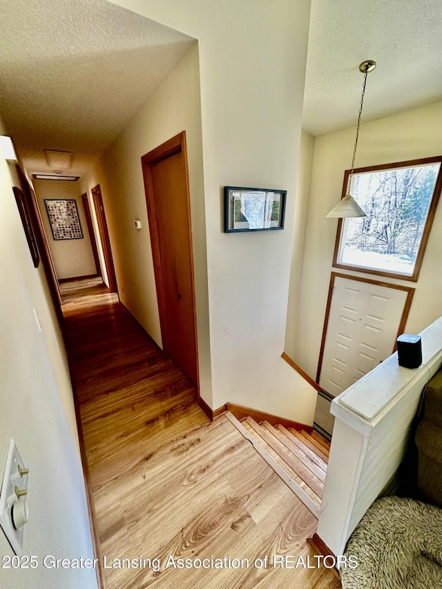 hallway with a textured ceiling, light wood-style floors, and baseboards