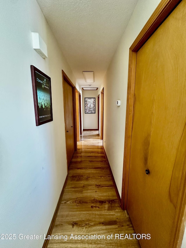 hallway with a textured ceiling, wood finished floors, and baseboards