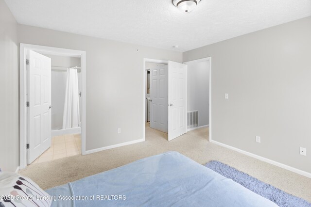 carpeted bedroom featuring visible vents, a textured ceiling, baseboards, and ensuite bath