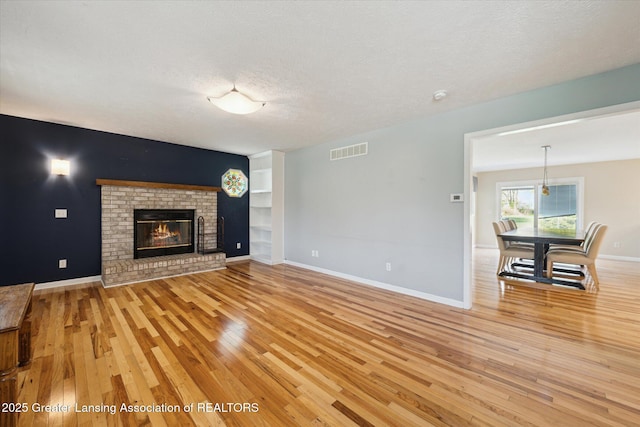 unfurnished living room featuring visible vents, a fireplace, baseboards, light wood-type flooring, and a textured ceiling