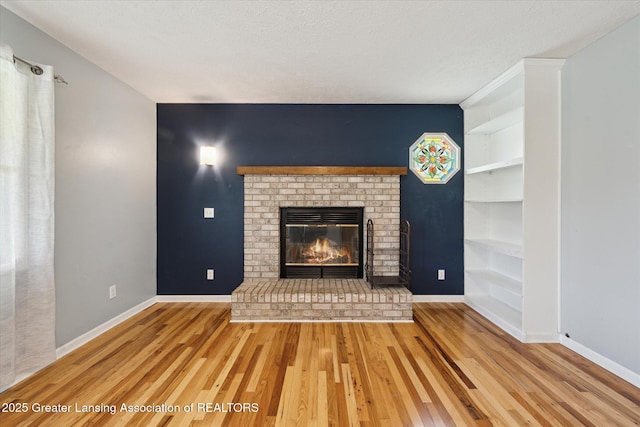 unfurnished living room featuring built in shelves, baseboards, a brick fireplace, and wood finished floors