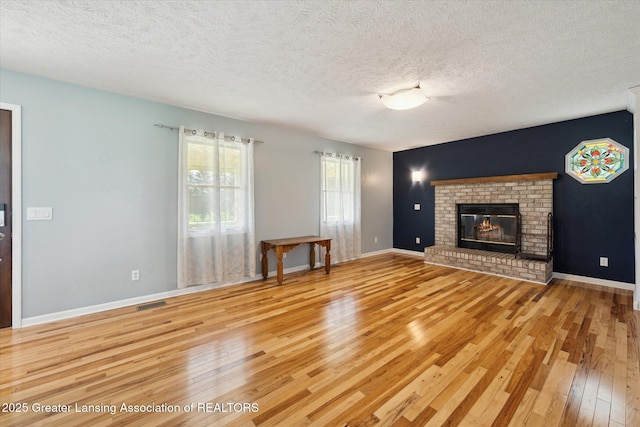 unfurnished living room featuring baseboards, a textured ceiling, light wood finished floors, and a brick fireplace