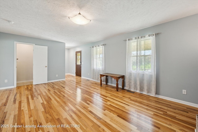 spare room with light wood-type flooring, a textured ceiling, and baseboards