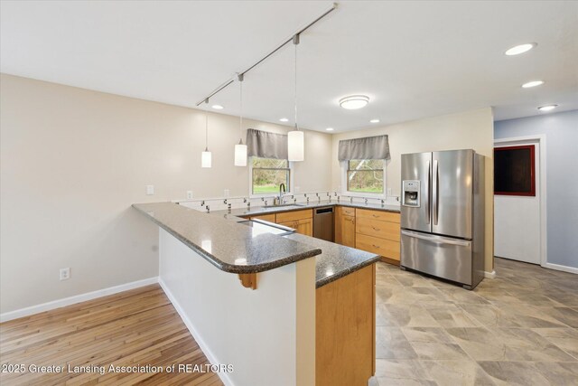 kitchen with a peninsula, baseboards, a sink, appliances with stainless steel finishes, and decorative light fixtures