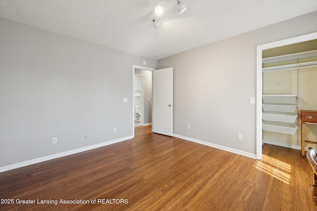 unfurnished bedroom featuring baseboards, wood finished floors, and a spacious closet