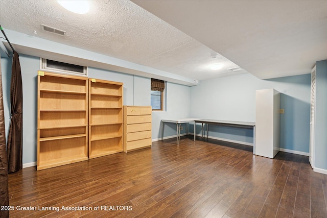 finished basement with baseboards, dark wood-style floors, a textured ceiling, and visible vents