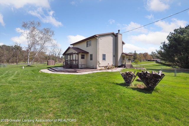 back of house featuring a chimney, a lawn, fence, an outdoor structure, and a storage unit