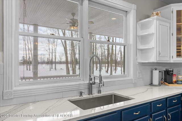 1785 N Williamston Rd, Williamston, MI 48895 - kitchen featuring light stone counters, white cabinetry, a sink, ceiling fan, and blue cabinetry