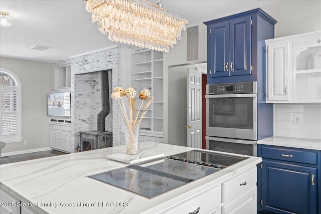 1785 N Williamston Rd, Williamston, MI 48895 - kitchen featuring blue cabinets, stainless steel double oven, black electric stovetop, an inviting chandelier, and a wood stove