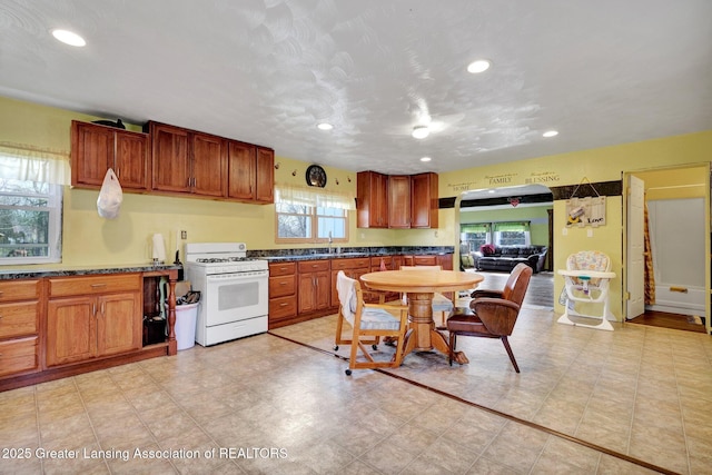 kitchen with white range with gas stovetop, dark countertops, and a wealth of natural light