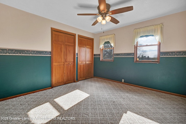 unfurnished bedroom featuring two closets, ceiling fan, light carpet, and baseboards