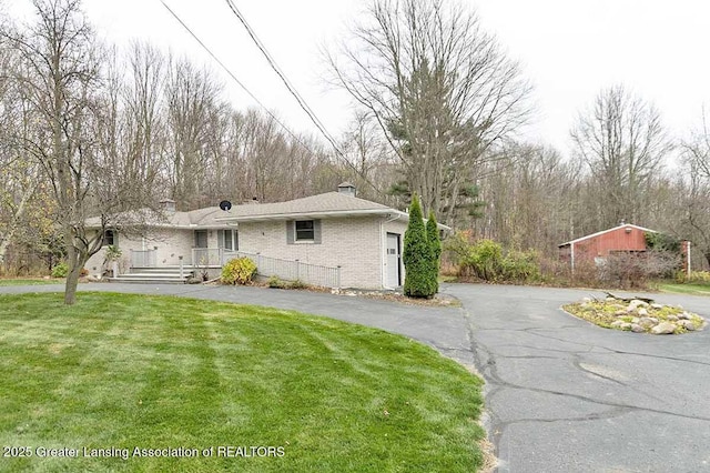 single story home featuring brick siding, driveway, a chimney, and a front lawn