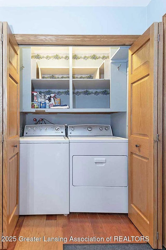 clothes washing area featuring laundry area, washer and clothes dryer, and wood finished floors