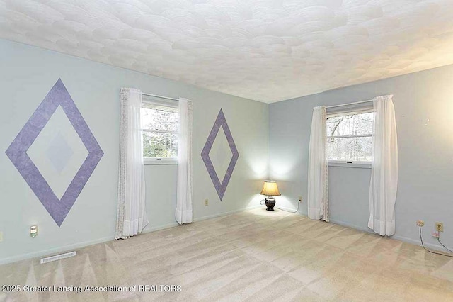 carpeted spare room featuring a textured ceiling, baseboards, and visible vents