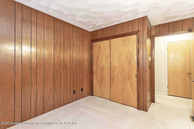 unfurnished bedroom featuring wood walls, carpet, and a closet