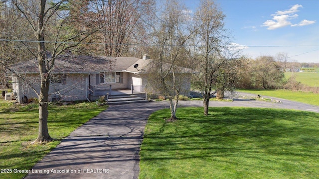 ranch-style house featuring a front lawn, aphalt driveway, covered porch, a chimney, and brick siding