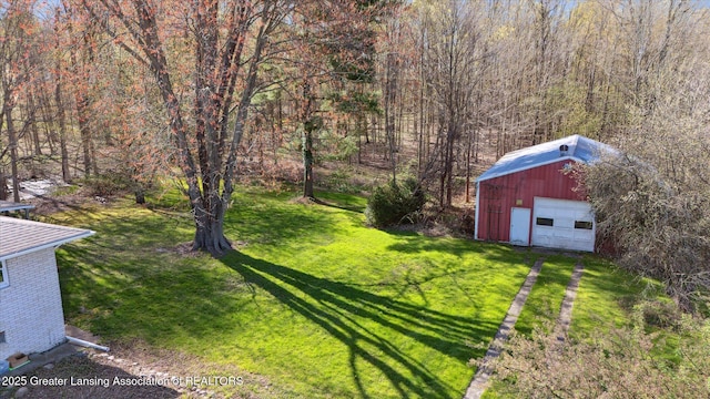 view of yard featuring a view of trees, driveway, an outbuilding, and a garage