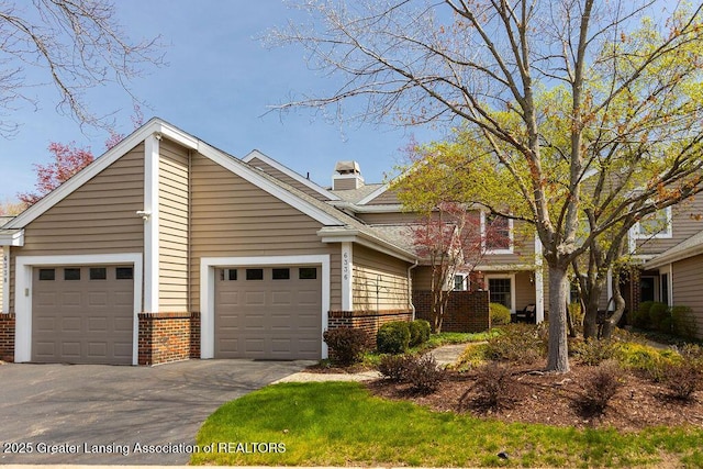 view of front of property featuring an attached garage, a chimney, driveway, and brick siding