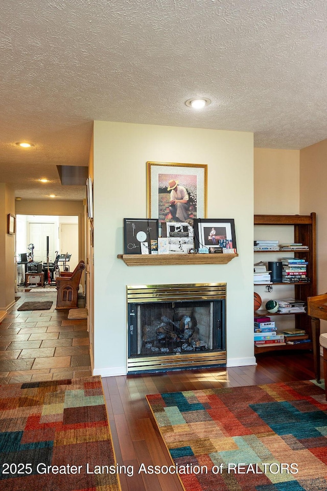 living room with a glass covered fireplace, baseboards, a textured ceiling, and wood finished floors