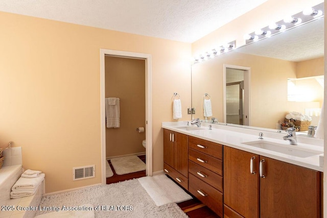 full bath with visible vents, a sink, double vanity, and toilet