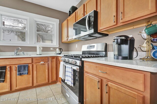 kitchen with brown cabinets, a sink, light tile patterned floors, light stone counters, and stainless steel appliances