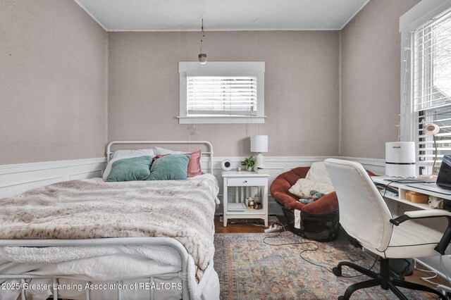 bedroom featuring multiple windows, wood finished floors, and a wainscoted wall