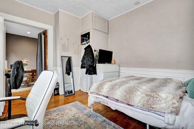 bedroom with crown molding, a wainscoted wall, a decorative wall, and wood finished floors