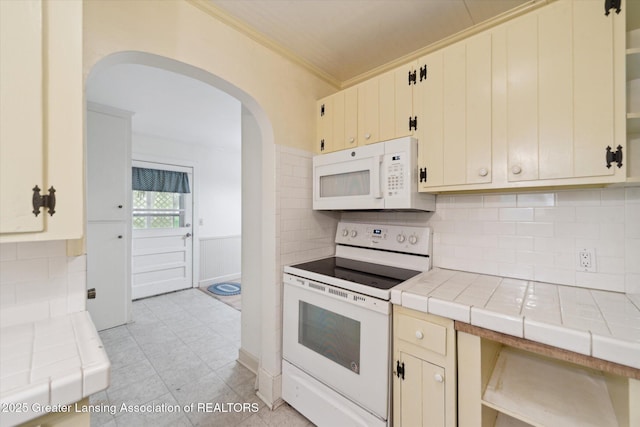 12102 Rupp Rd, Grand Ledge, MI 48837 - kitchen with white appliances, tile counters, arched walkways, ornamental molding, and cream cabinetry
