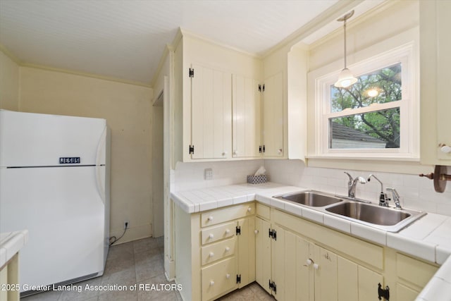 12102 Rupp Rd, Grand Ledge, MI 48837 - kitchen with freestanding refrigerator, a sink, ornamental molding, cream cabinets, and tile counters
