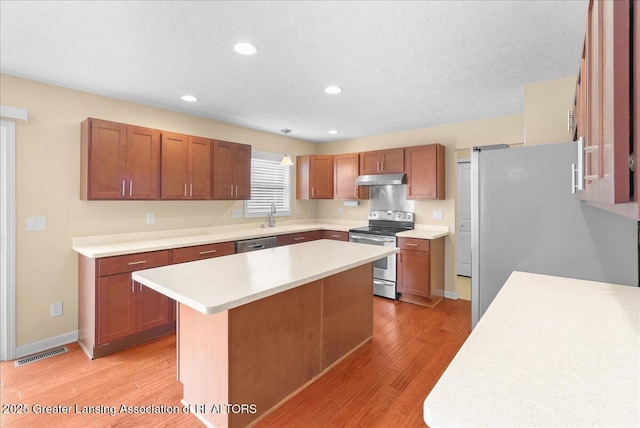 609 E Avocet Dr, East Lansing, MI 48823 - kitchen with appliances with stainless steel finishes, under cabinet range hood, light wood-style floors, light countertops, and a center island