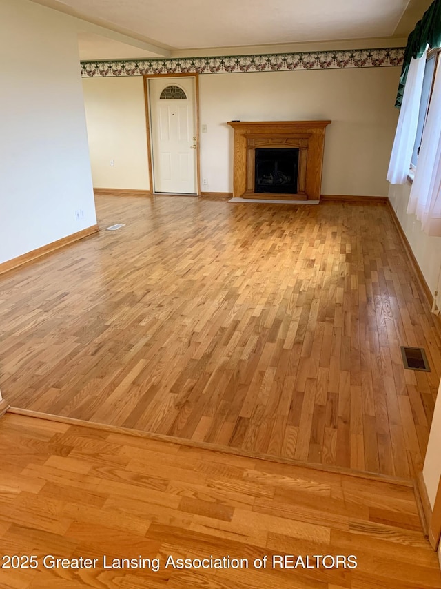 3156 E M-21 Rd, Saint Johns, MI 48879 - unfurnished living room featuring light wood-style floors, a fireplace with raised hearth, visible vents, and baseboards
