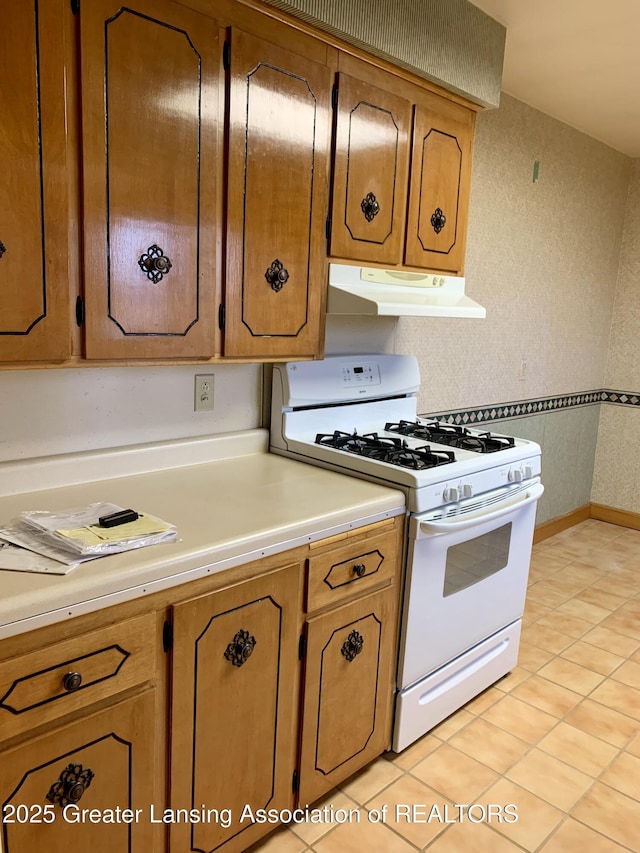 3156 E M-21 Rd, Saint Johns, MI 48879 - kitchen featuring brown cabinets, under cabinet range hood, white range with gas cooktop, light tile patterned flooring, and light countertops