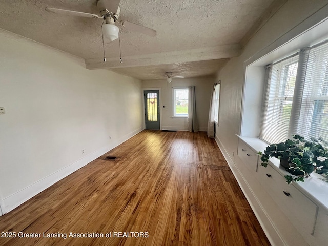 interior space featuring a textured ceiling, ceiling fan, visible vents, baseboards, and wood finished floors