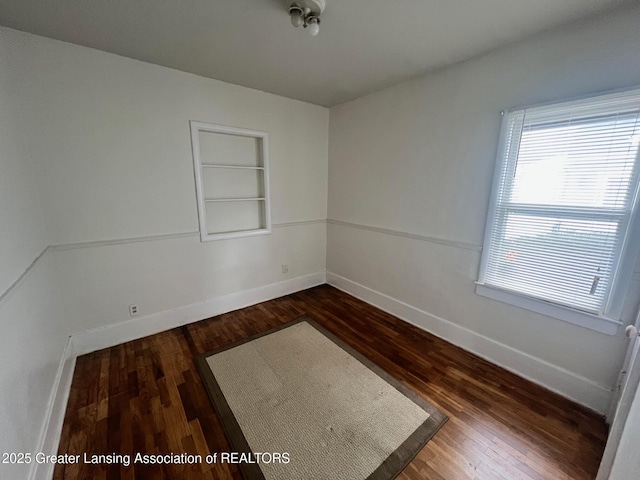 empty room with baseboards, built in features, and dark wood-style flooring