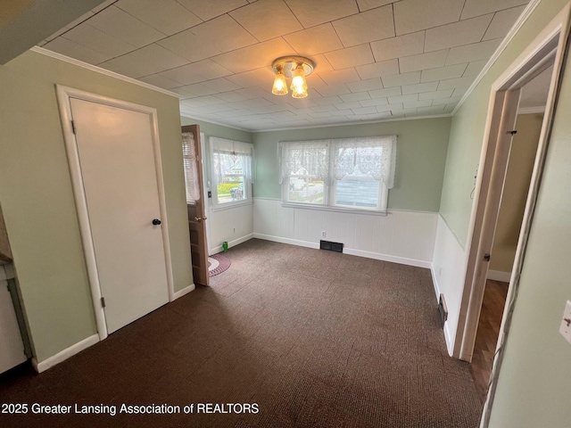 unfurnished bedroom featuring dark carpet, a wainscoted wall, and crown molding