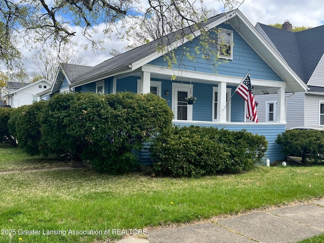 bungalow with a front lawn, a shingled roof, and covered porch