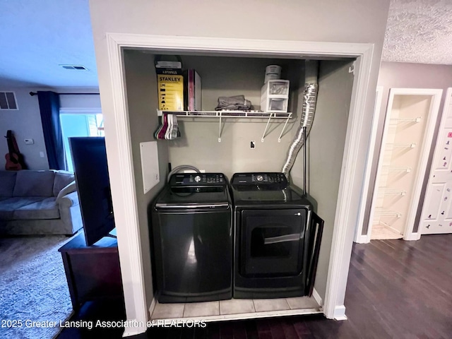 clothes washing area with washer and dryer, visible vents, laundry area, and wood finished floors