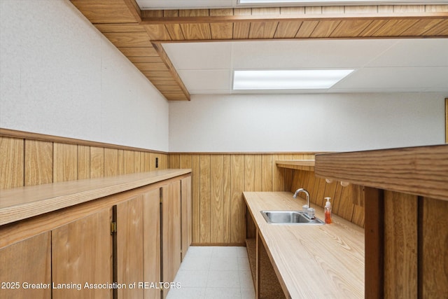 kitchen featuring a sink, wood walls, light countertops, brown cabinetry, and wainscoting