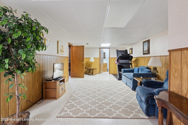 interior space featuring wood walls, a drop ceiling, and a wainscoted wall