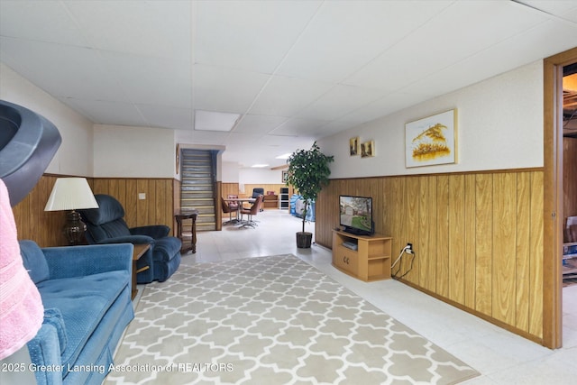 living room with tile patterned floors, wooden walls, a drop ceiling, and wainscoting