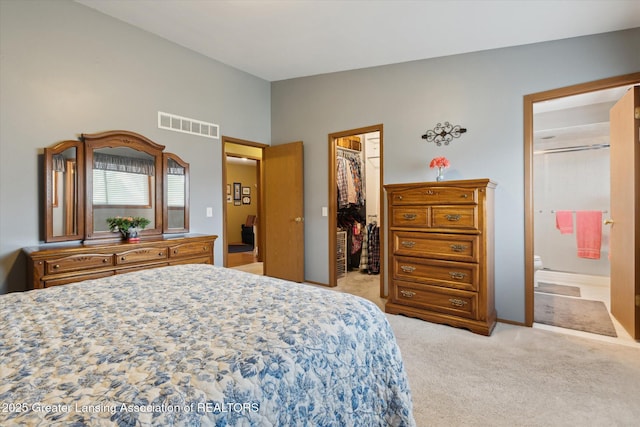 bedroom featuring a closet, light carpet, a walk in closet, visible vents, and lofted ceiling