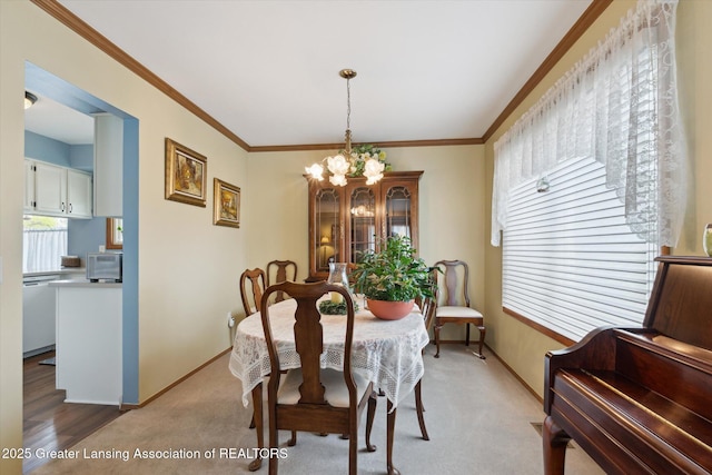 dining room with crown molding, a notable chandelier, light carpet, and baseboards