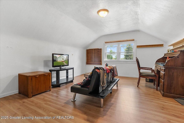 interior space with light wood-style flooring, a textured ceiling, vaulted ceiling, and baseboards