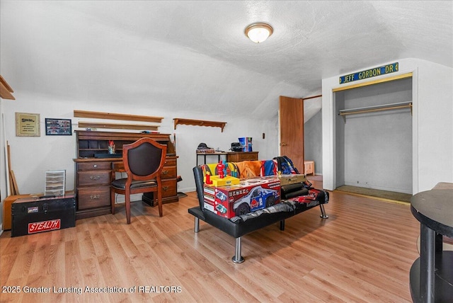 bedroom with wood finished floors, vaulted ceiling, a closet, and a textured ceiling