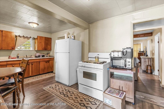 kitchen featuring white appliances, brown cabinets, dark wood finished floors, light countertops, and a sink