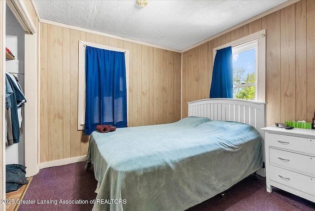 bedroom featuring wood walls, a textured ceiling, baseboards, and dark colored carpet